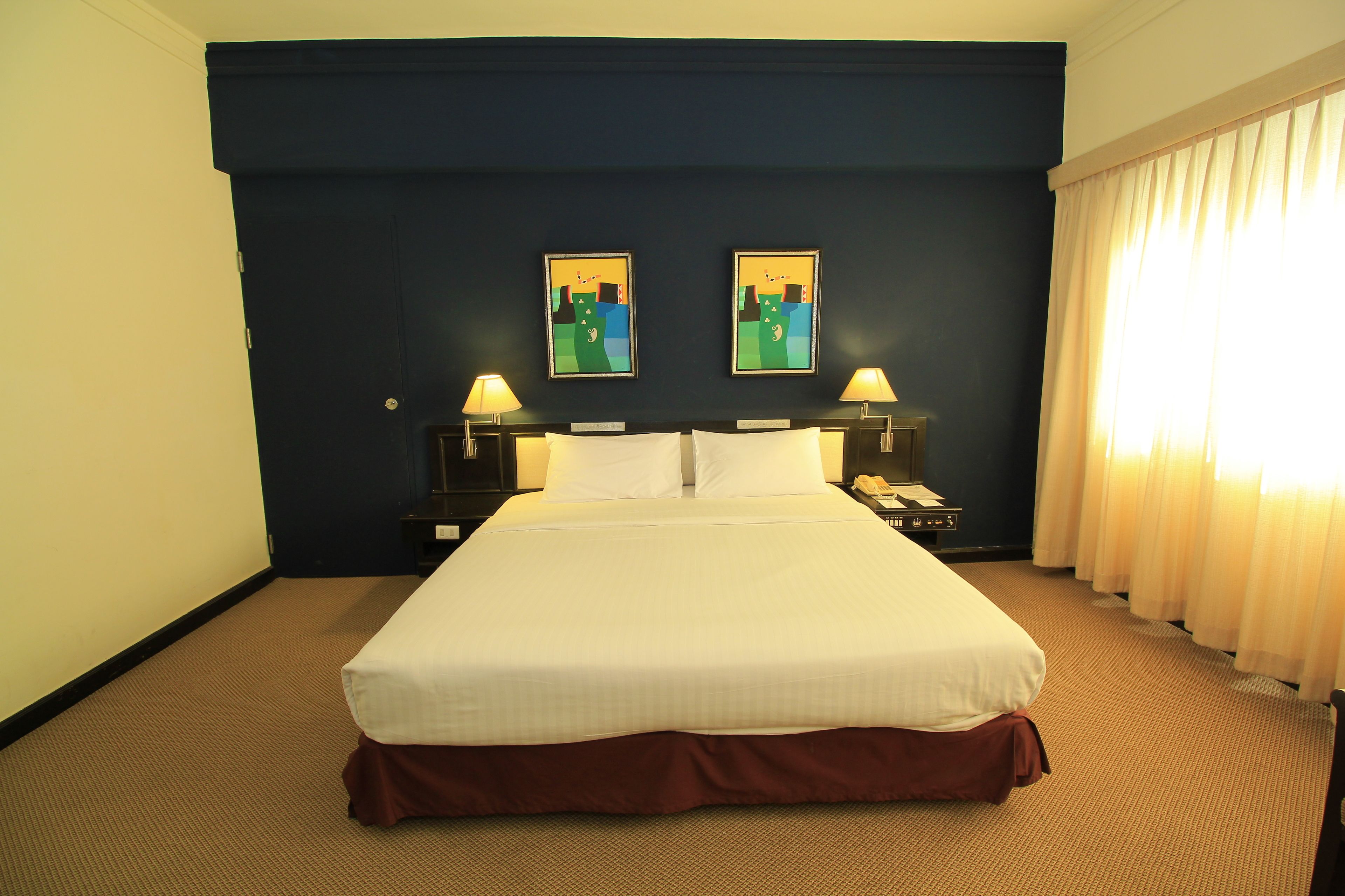 A hotel room with a large bed, two bedside tables with lamps, and two framed artworks on the wall.