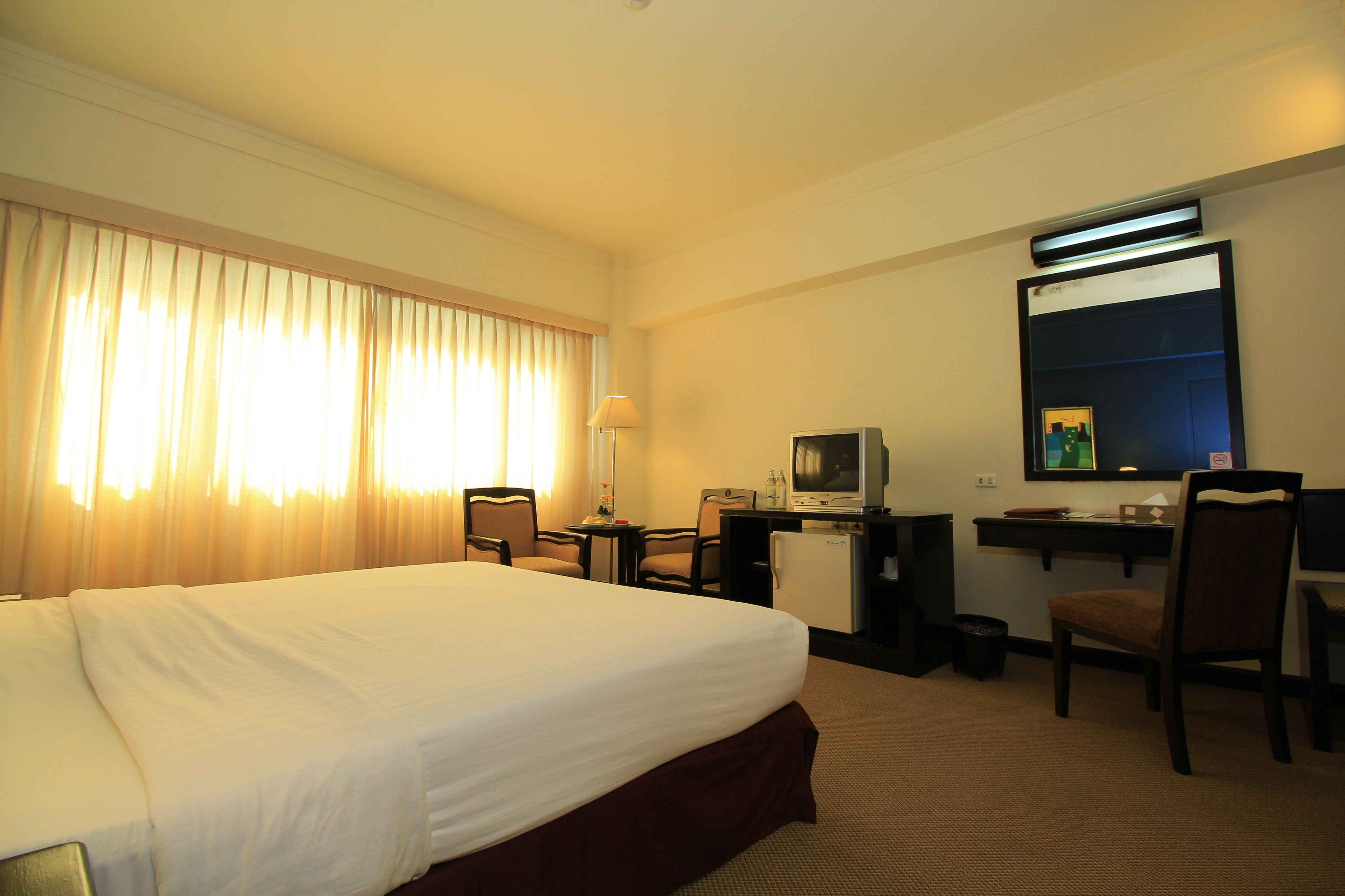 A hotel room with a large bed, a desk with a computer, a chair, and a television.