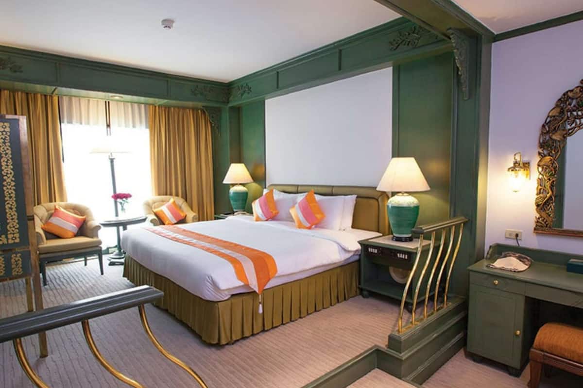 A hotel room with a large bed, two bedside tables with lamps, a desk with a chair, a mirror, and a window with curtains.
