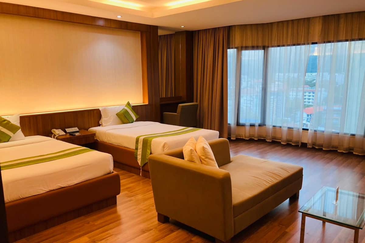 A hotel room with two beds, a sofa, a glass coffee table, and a view of the city through large windows.