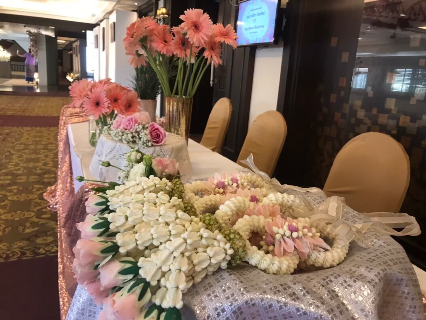 Una mesa adornada con diversas flores y un centro de mesa decorativo, con una pantalla de televisión al fondo.