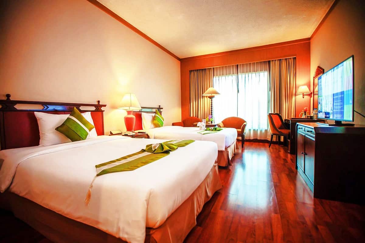 A hotel room with two beds, a desk, a chair, and a television.