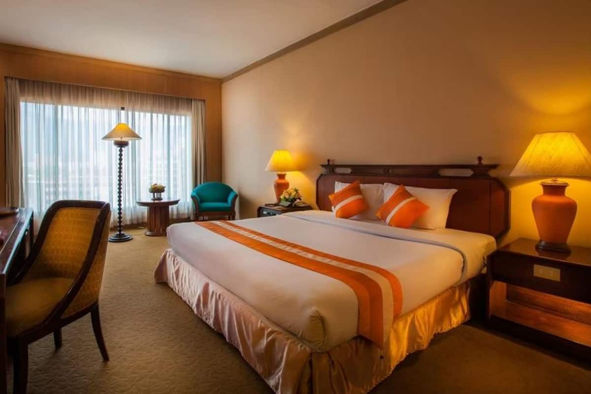 A hotel room with a large bed, two bedside lamps, a chair, a small table, and a window with curtains.