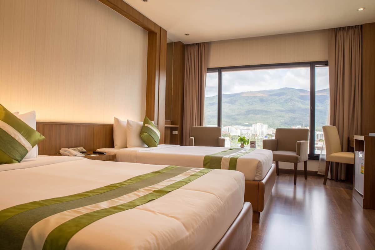 A hotel room with two beds, a desk, a chair, and a large window with a city view.