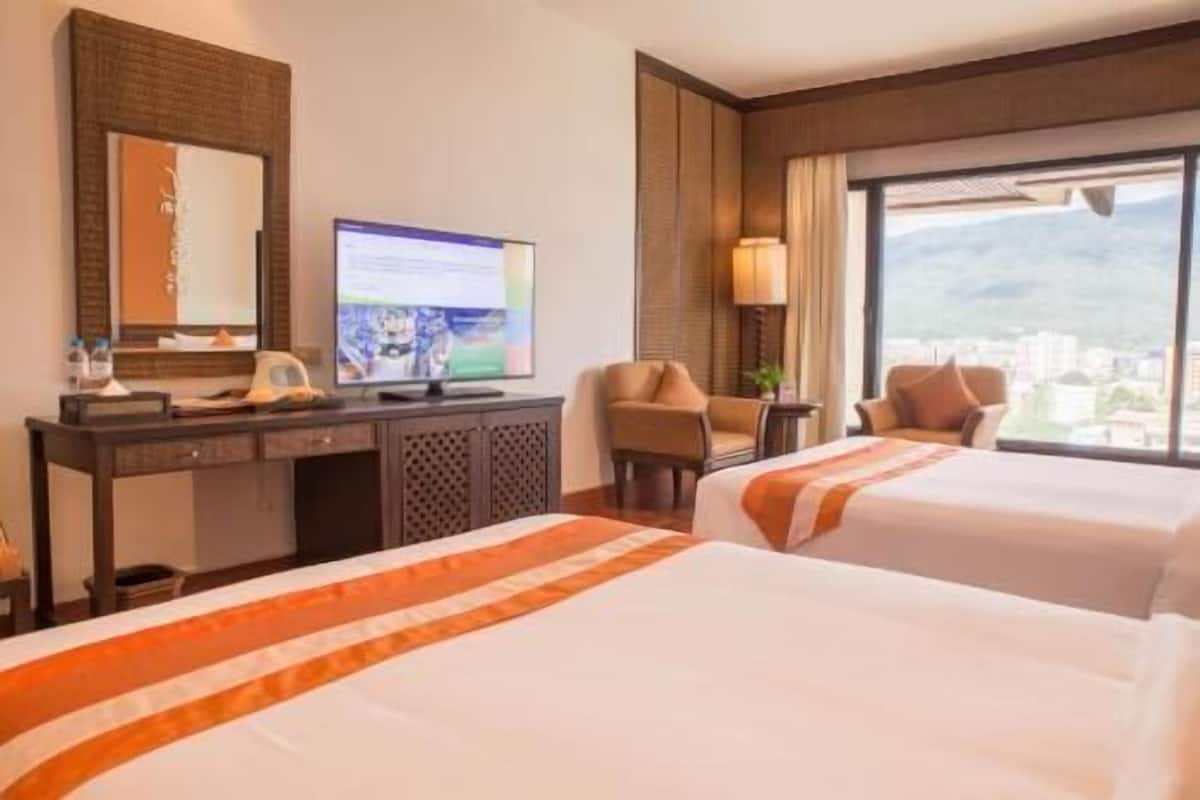 A hotel room with two beds, a desk with a computer, a chair, and a large window with a view.