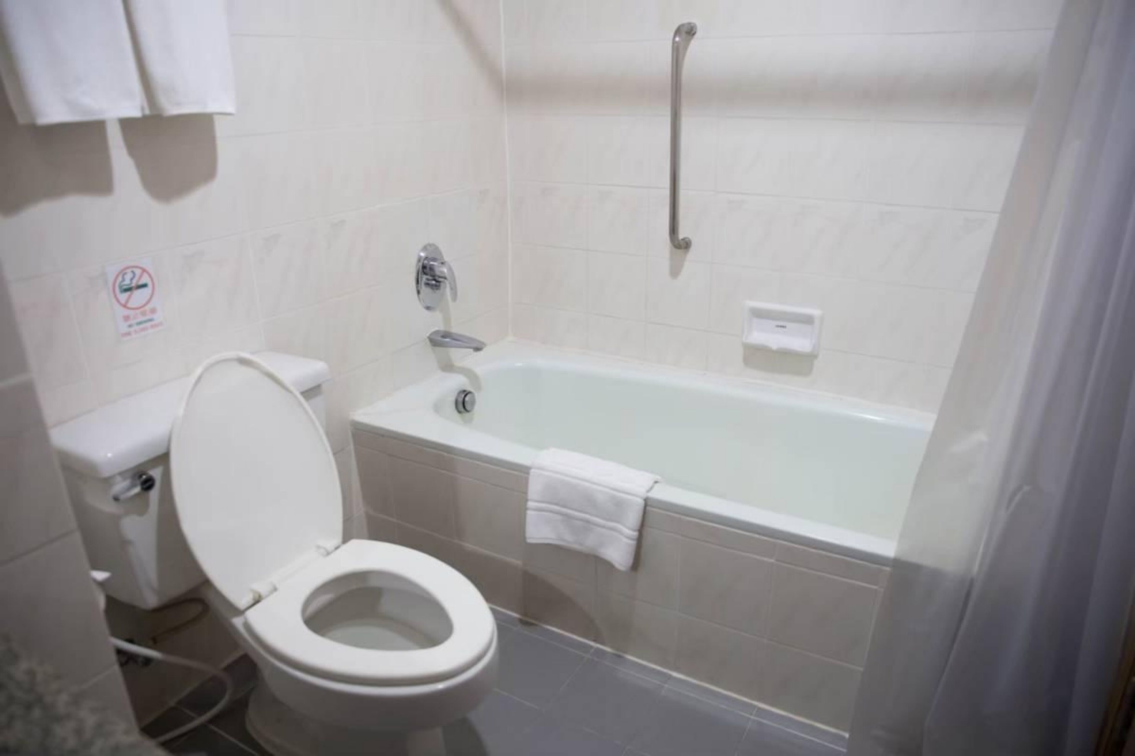 A bathroom with a toilet, a bathtub, and a handrail.