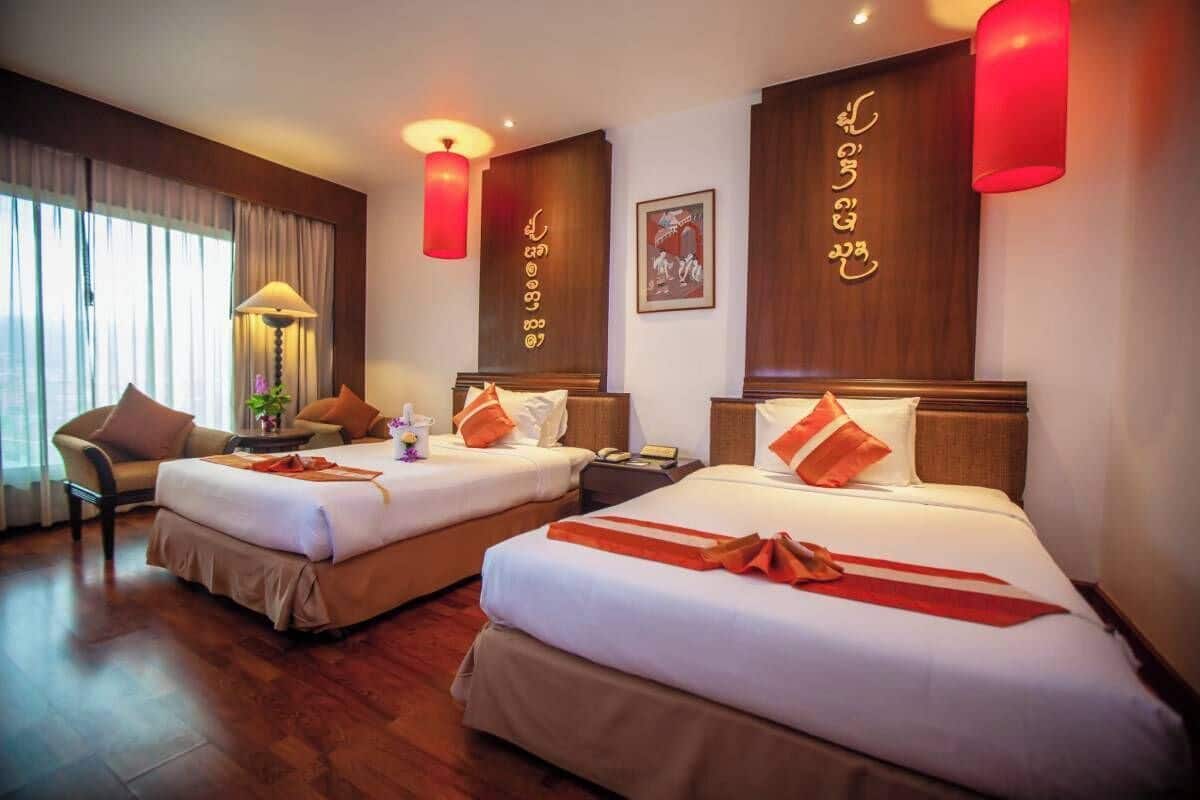 A hotel room with two beds, a sitting area with a chair, a lamp, and a wall with decorative elements.