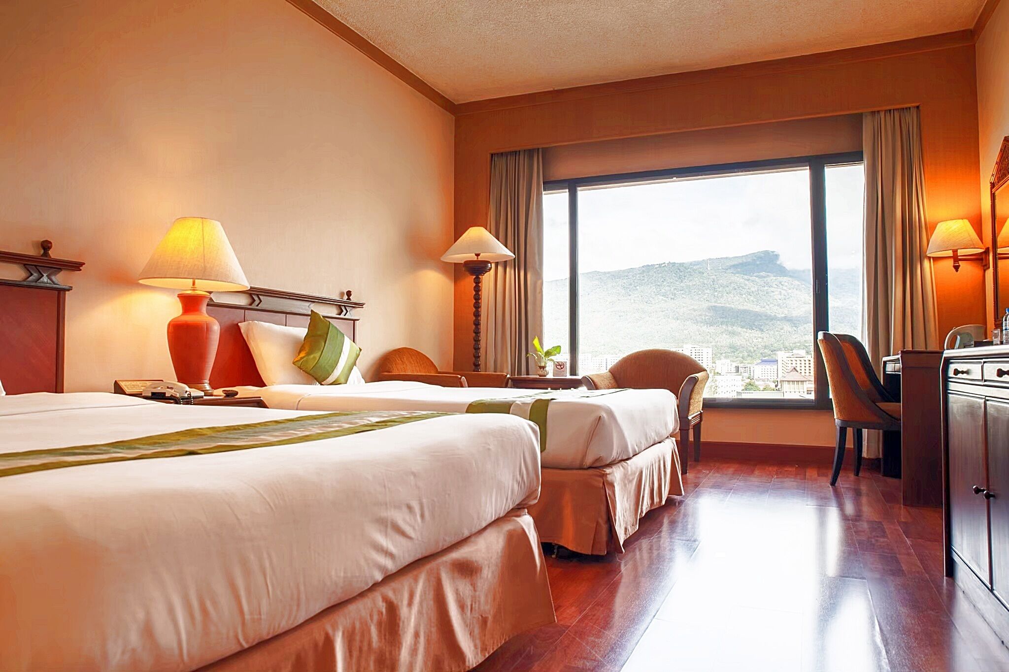 A hotel room with two beds, a desk, and a view of a mountainous landscape.