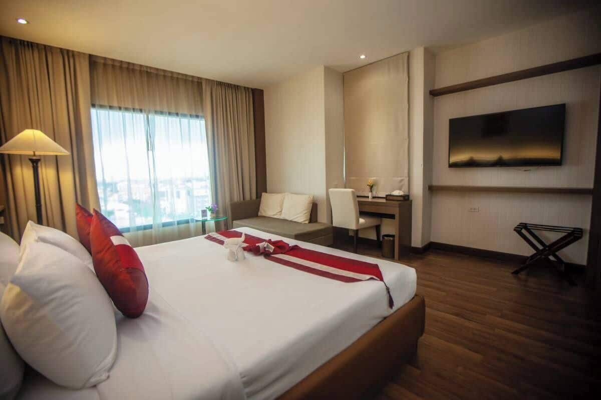 A hotel room with a large bed, a desk, a chair, a TV, and a view of the city.
