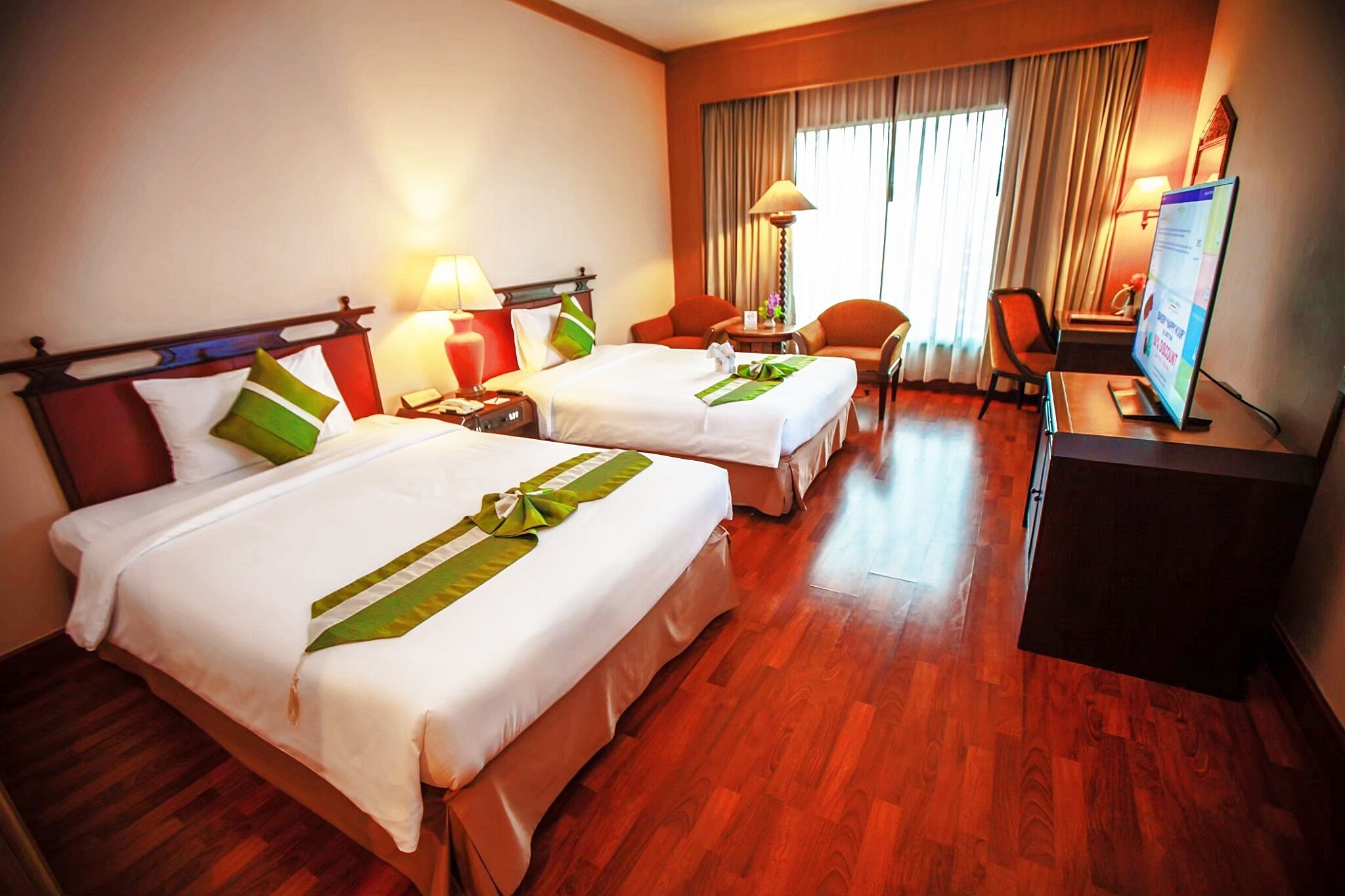 A hotel room with two beds, a desk, a chair, a television, and a window with curtains.