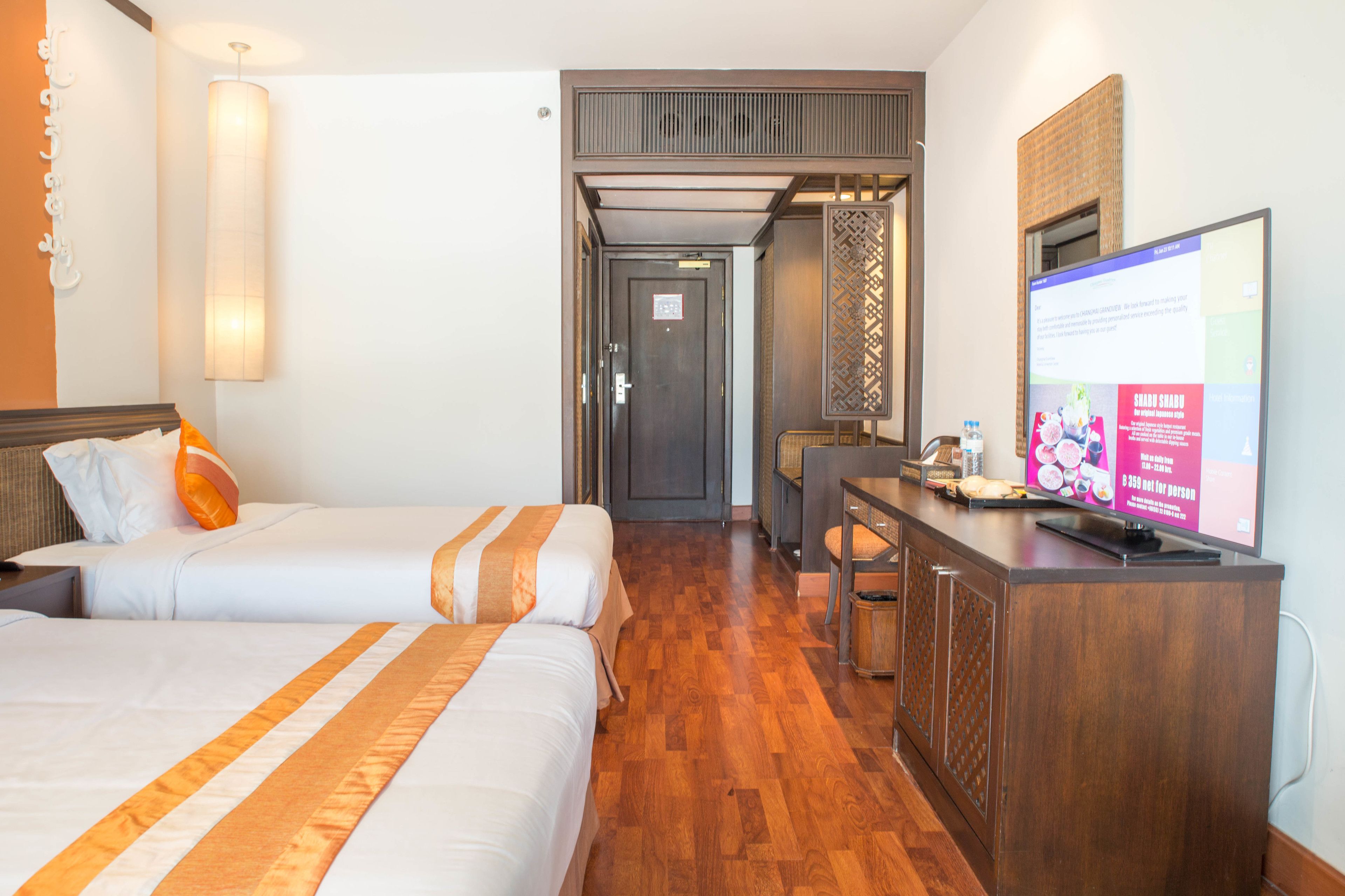 A hotel room with two beds, a wooden desk, a television, and a view of the hallway.