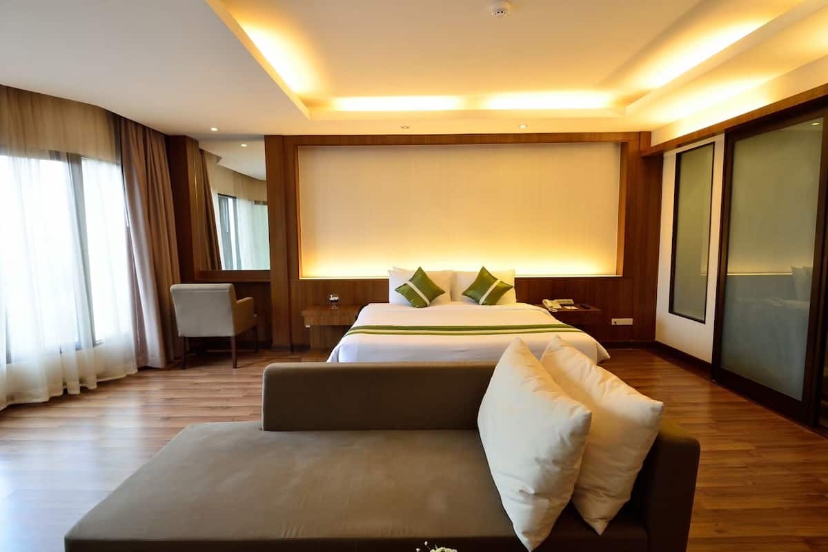 A modern hotel room with a large bed, a sofa, a desk, and a large window with curtains.