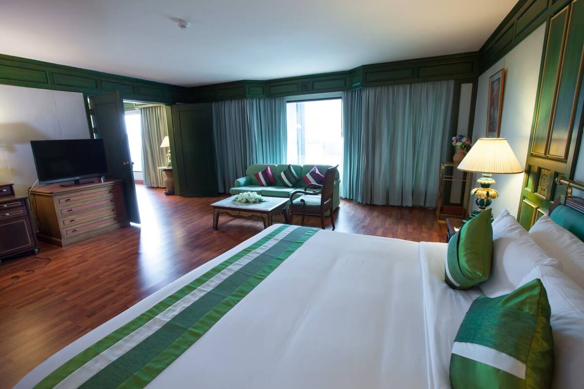 A hotel room with a large bed, a sofa, a television, a desk, and a lamp.