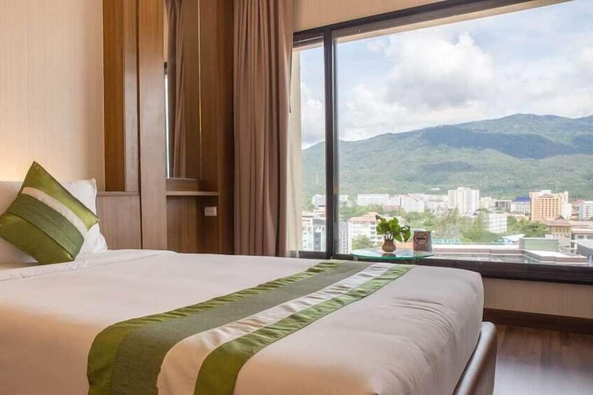 A hotel room with a large bed, a view of a cityscape and mountains, and a window with curtains.