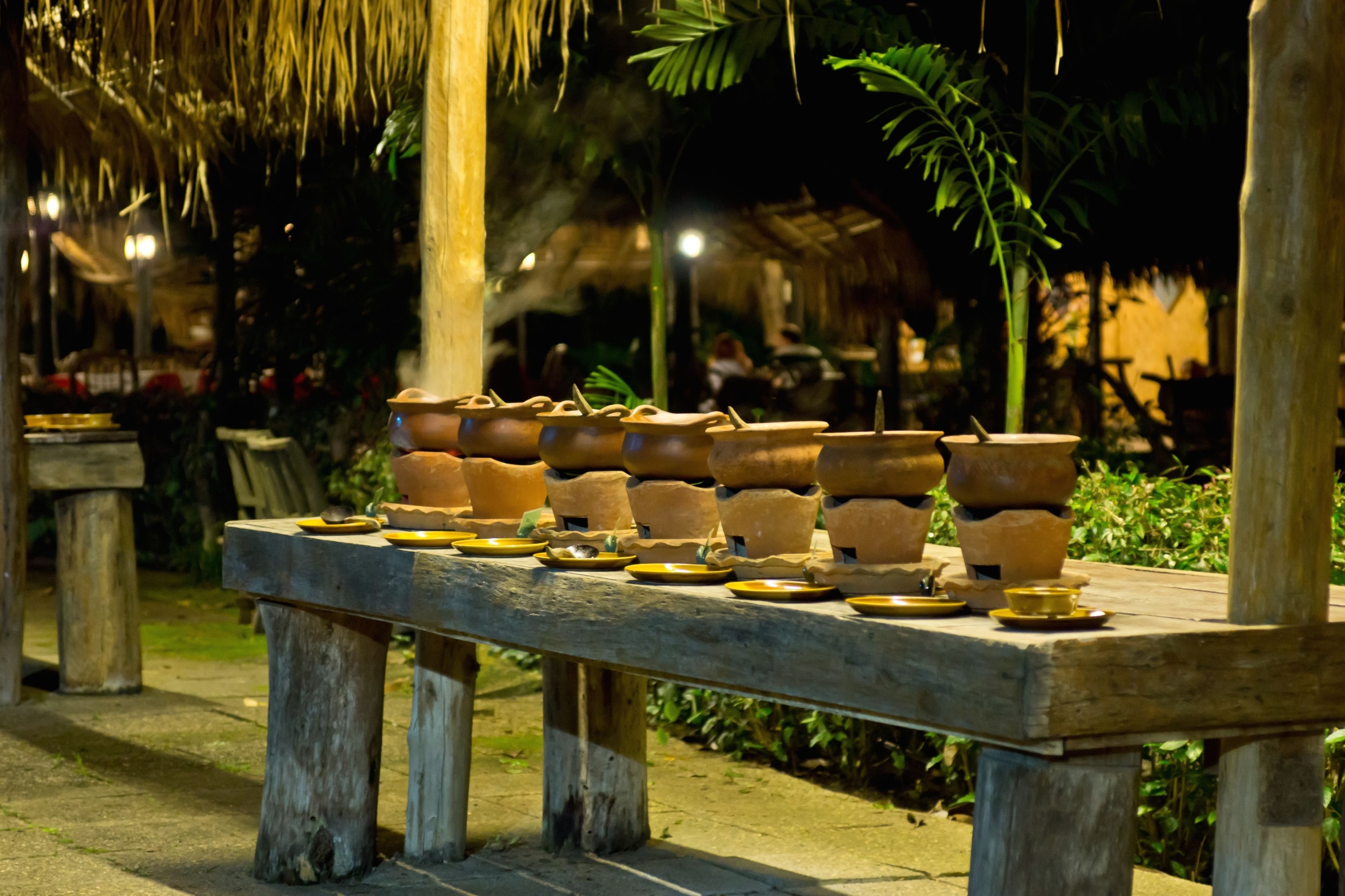 Una mesa de madera con macetas de terracota y platos, dispuesta al aire libre por la noche.