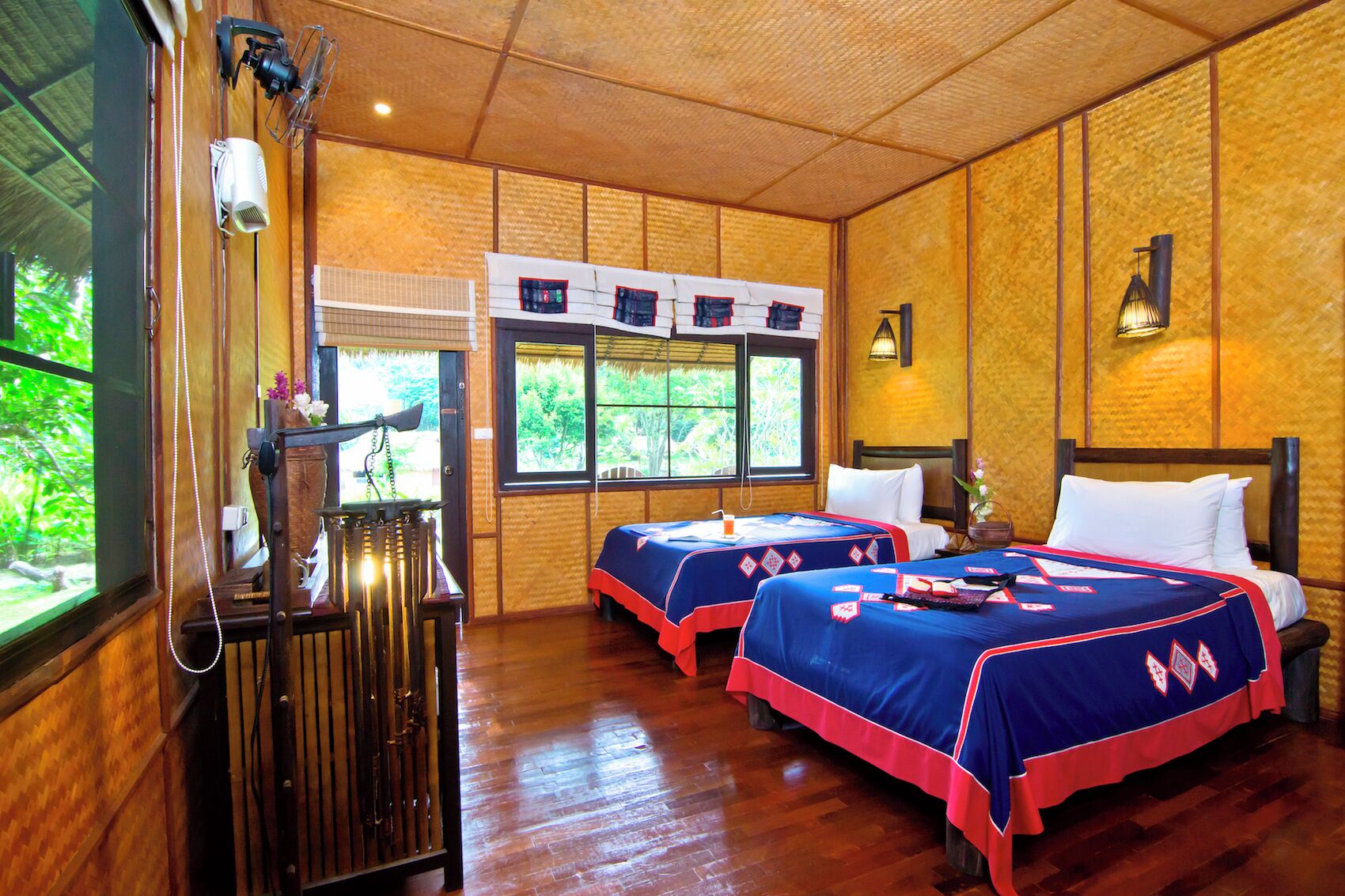 A room with two beds, wooden walls, a large window, and a wooden desk with a telephone.