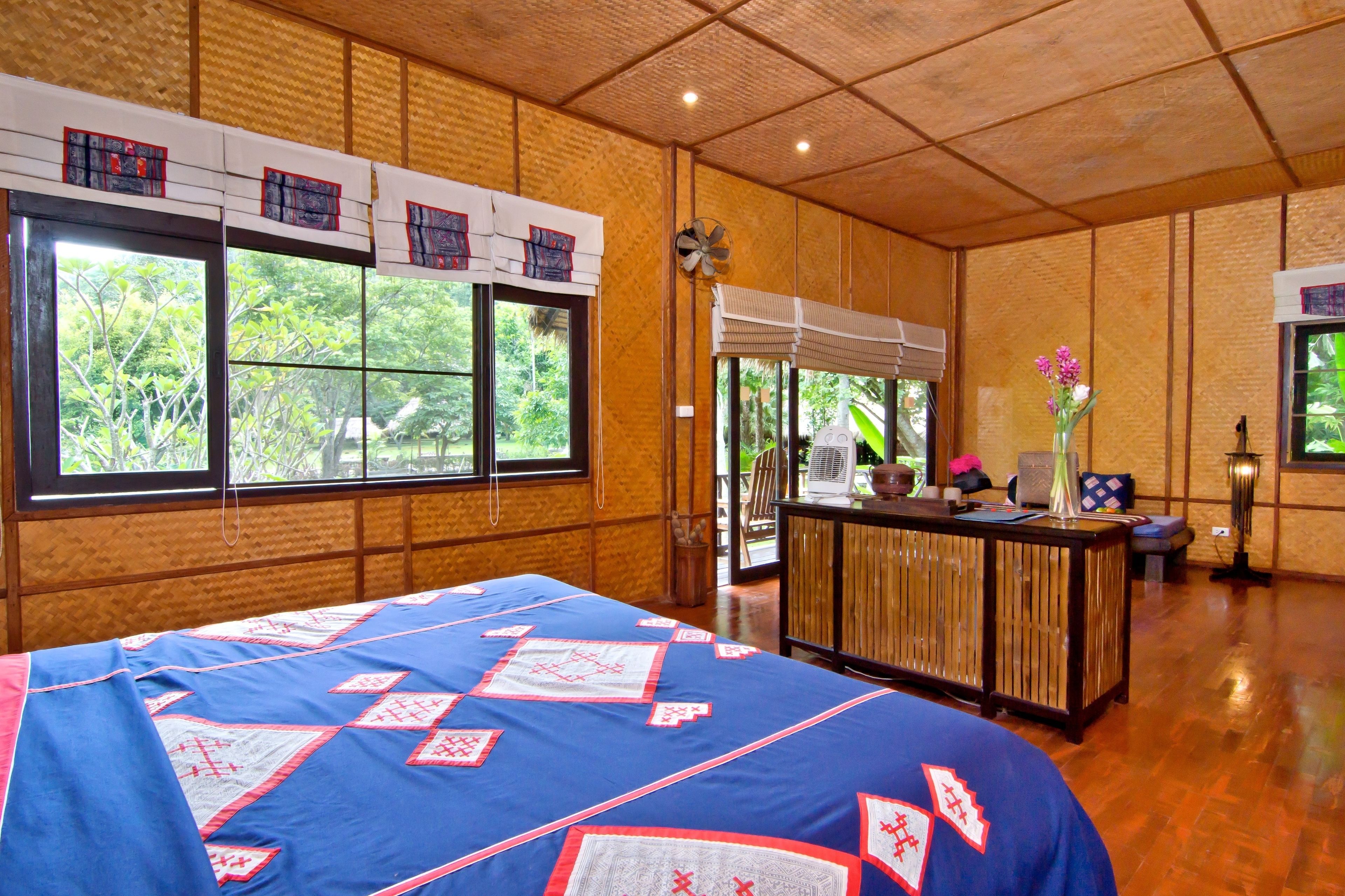 Una habitación con una cama grande, un escritorio de madera y ventanas amplias con vistas a zonas verdes.