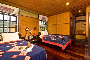A room with two beds, wooden flooring, a window with a view, and a door leading to another room.