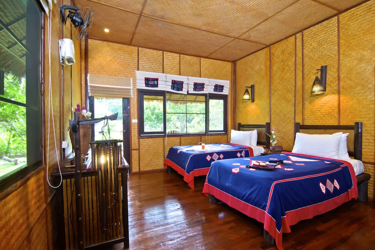 A room with two beds, wooden floors, a radiator, and a window with a view of greenery.