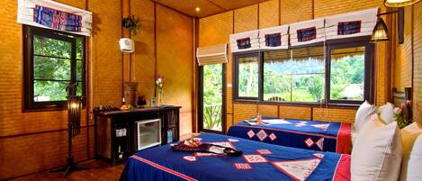 A room with two beds, wooden walls, large windows, a desk, and a fan.