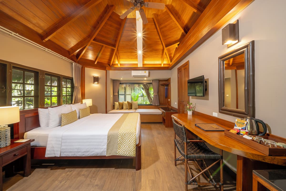 A hotel room with a wooden ceiling, a large bed with a patterned bedspread, a desk with a tray of snacks, and a large mirror.