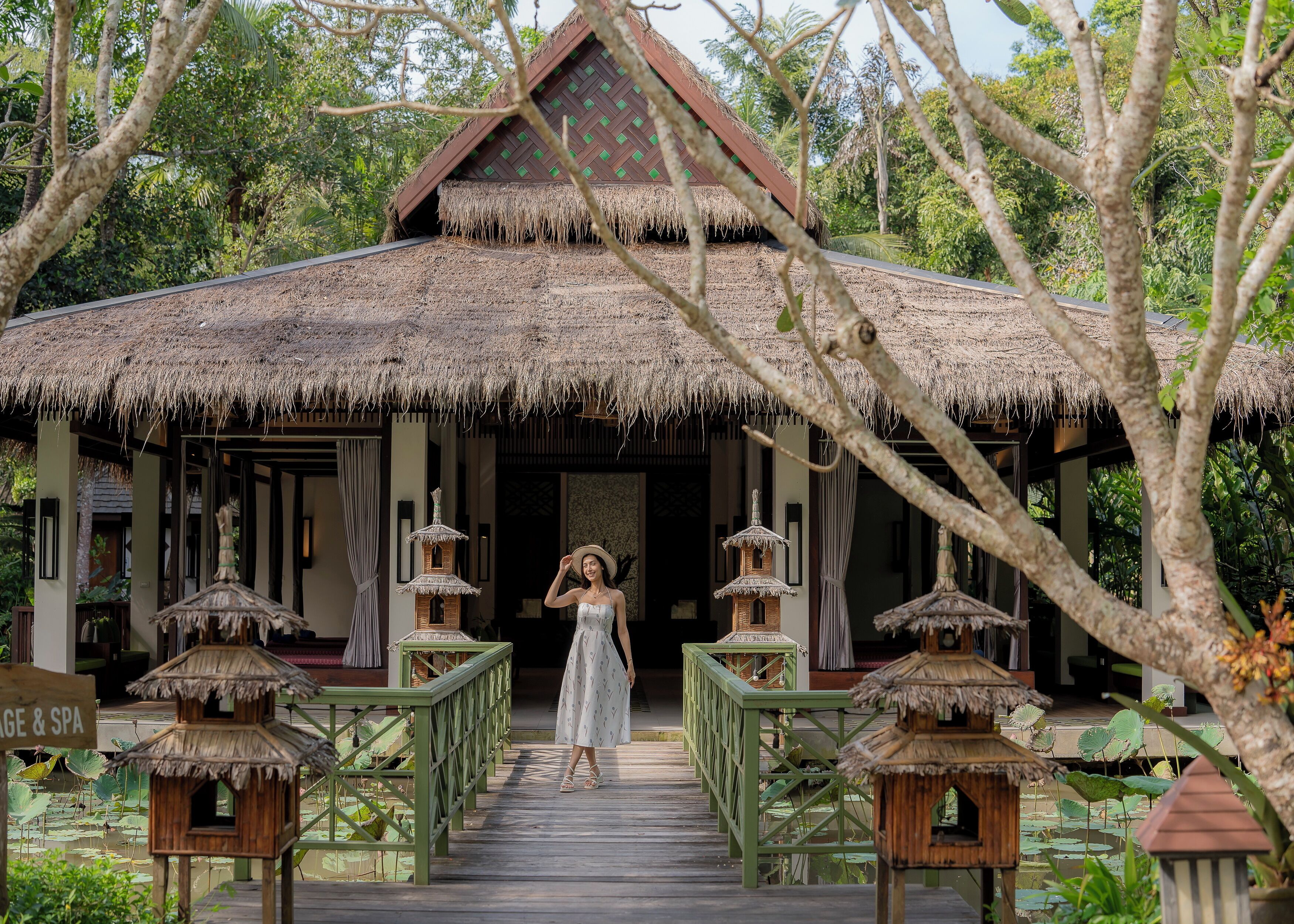 A traditional thatched-roof structure with a wooden deck leading to it, surrounded by lush greenery.