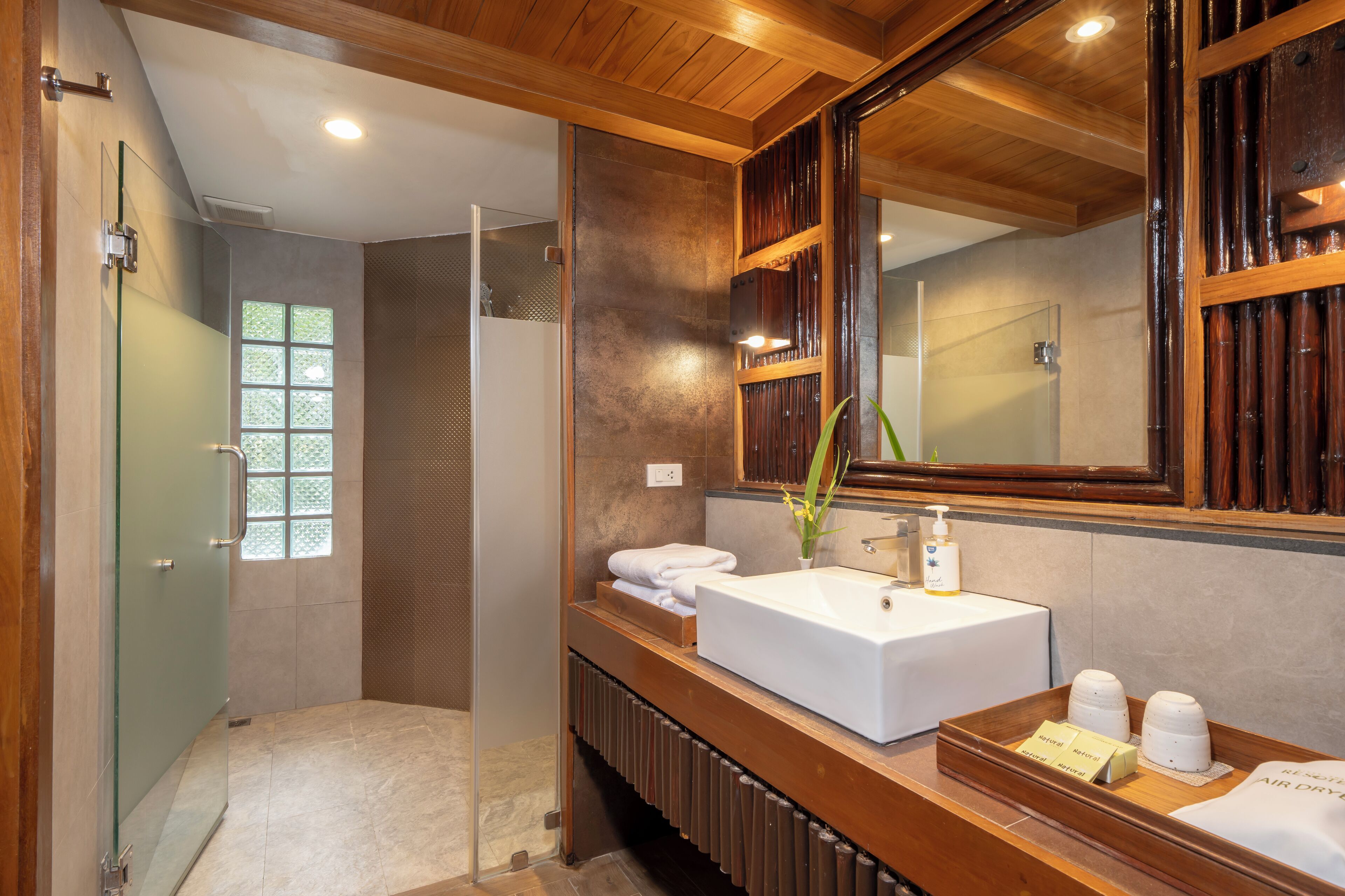 A modern bathroom with a wooden vanity, a large mirror, and a glass shower enclosure.