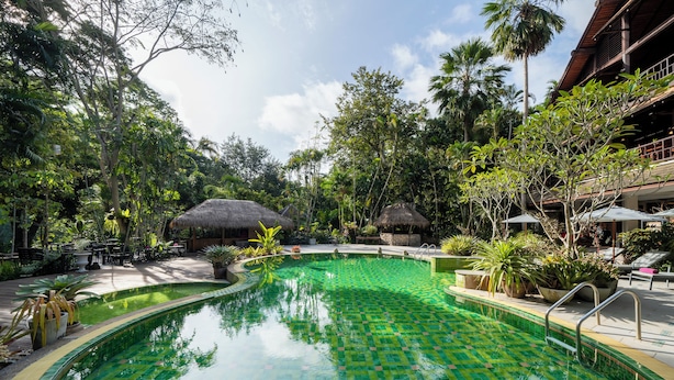 Una piscina con un estampado verde a cuadros, rodeada de abundante vegetación y palmeras.