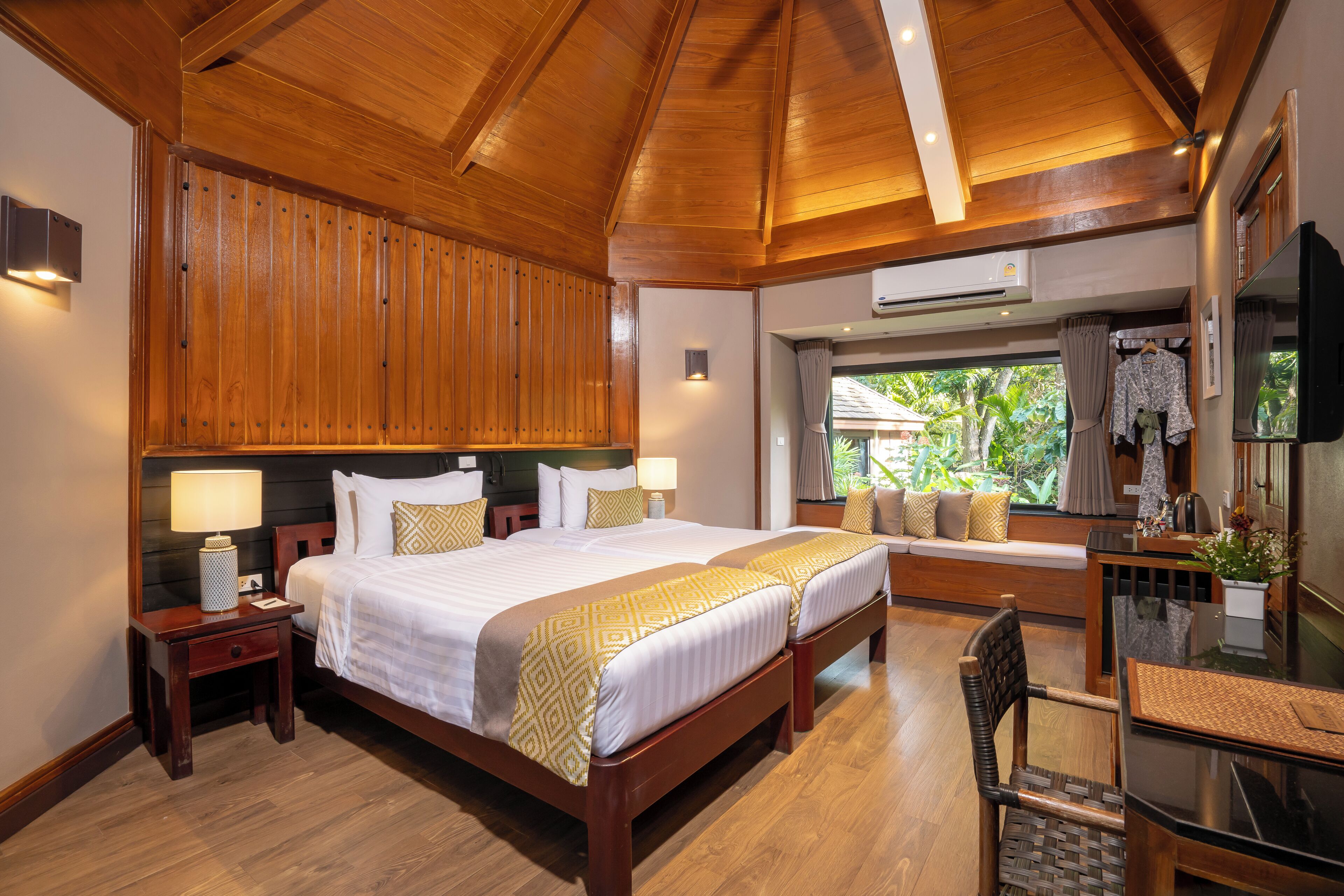 A spacious bedroom with a large bed, wooden ceiling, and a window with a view of greenery.