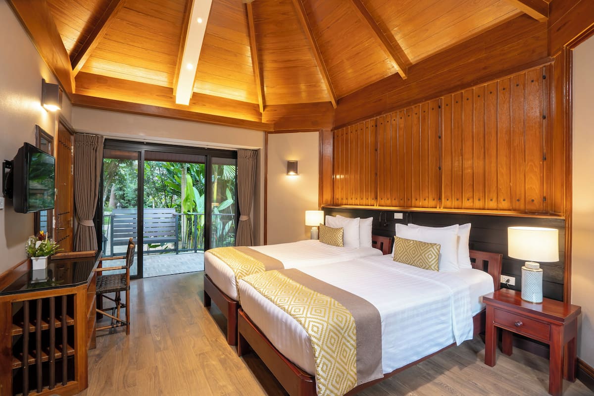 A hotel room with a large bed, a desk with a chair, a television, and a sliding glass door leading to an outdoor area.