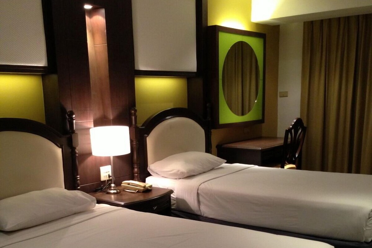 A hotel room with two beds, a nightstand with a lamp, a chair, and a wall-mounted TV.