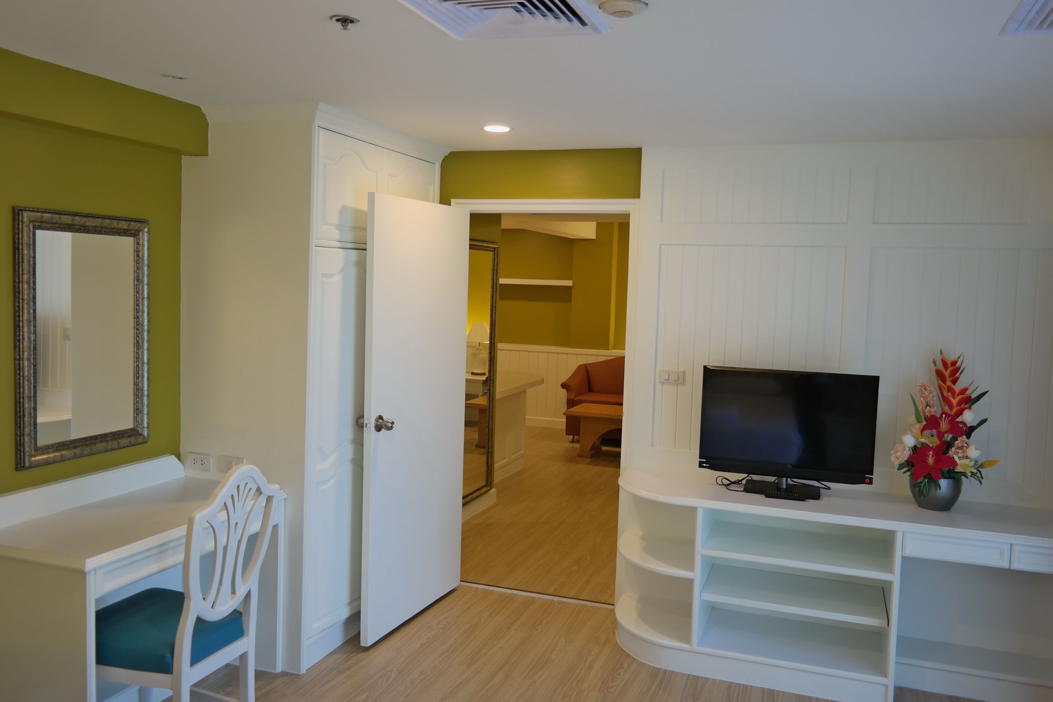 A room with a white desk, a chair, a television on a stand, and a door leading to another room.
