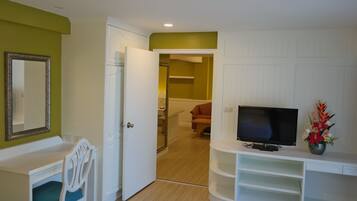 A room with a white desk, a chair, a television on a stand, and a door leading to another room.