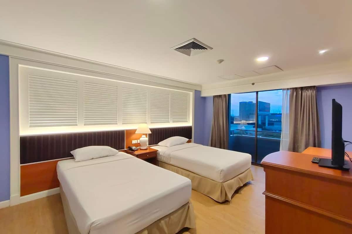 A hotel room with two beds, a desk, a lamp, and a television.