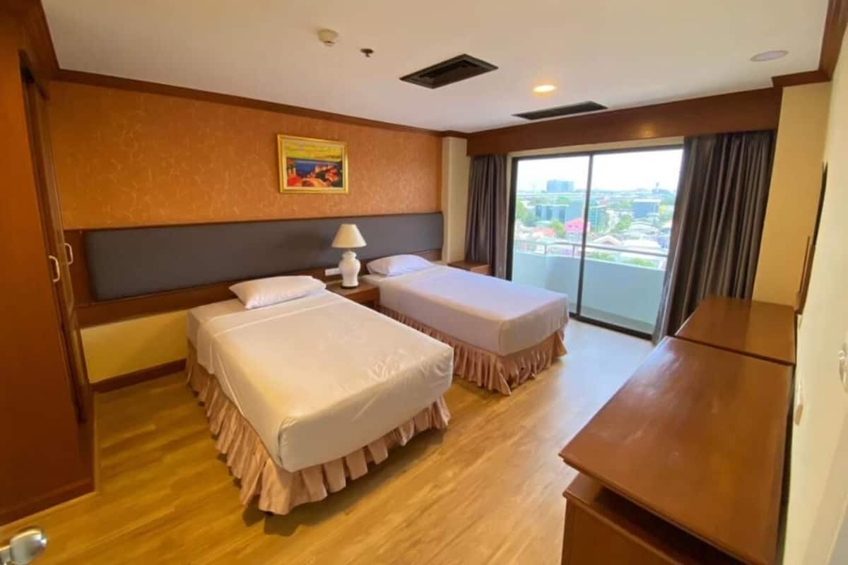 A hotel room with two beds, a desk, a lamp, and a large window with a city view.
