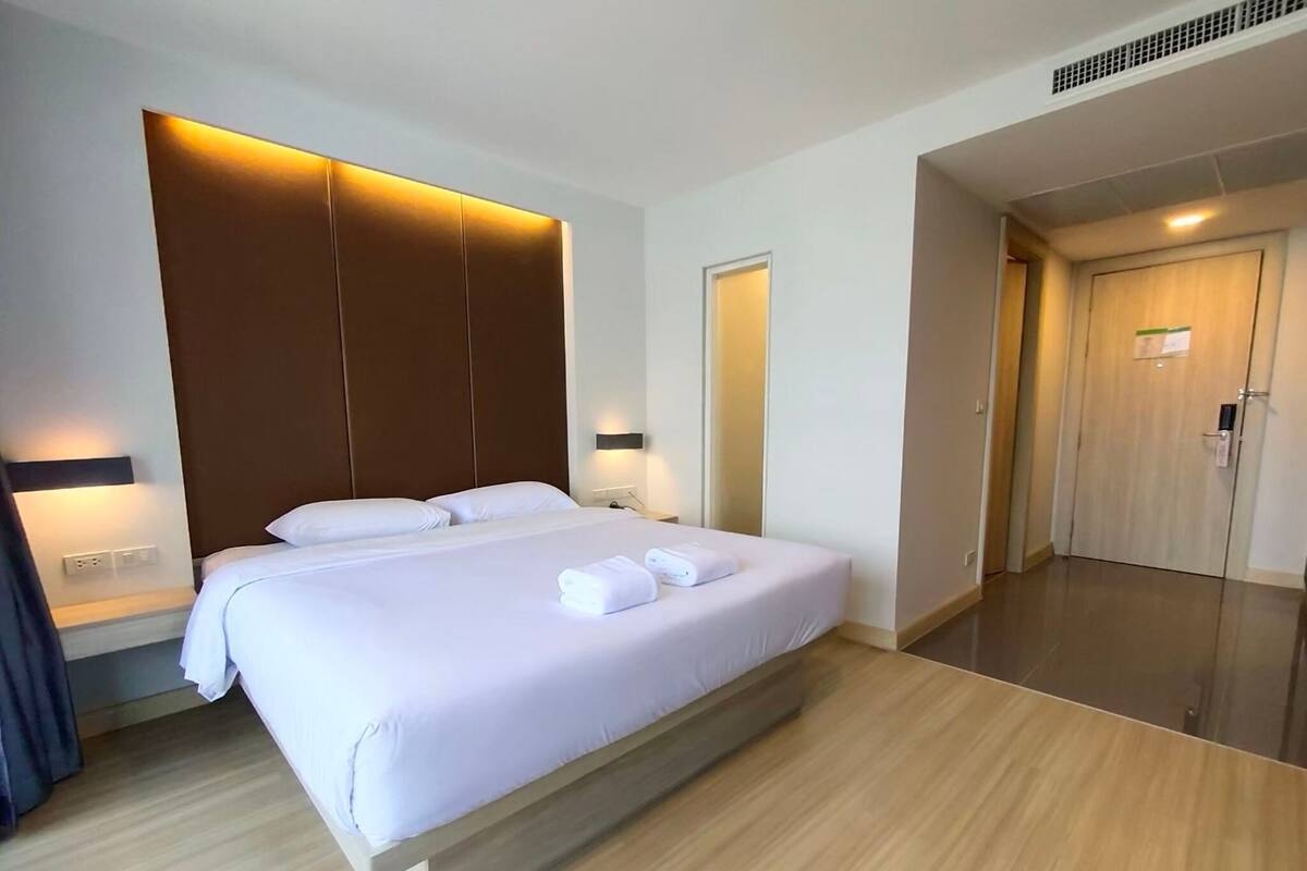 A modern hotel room with a large bed, wooden headboard, bedside lamps, and a wooden floor.