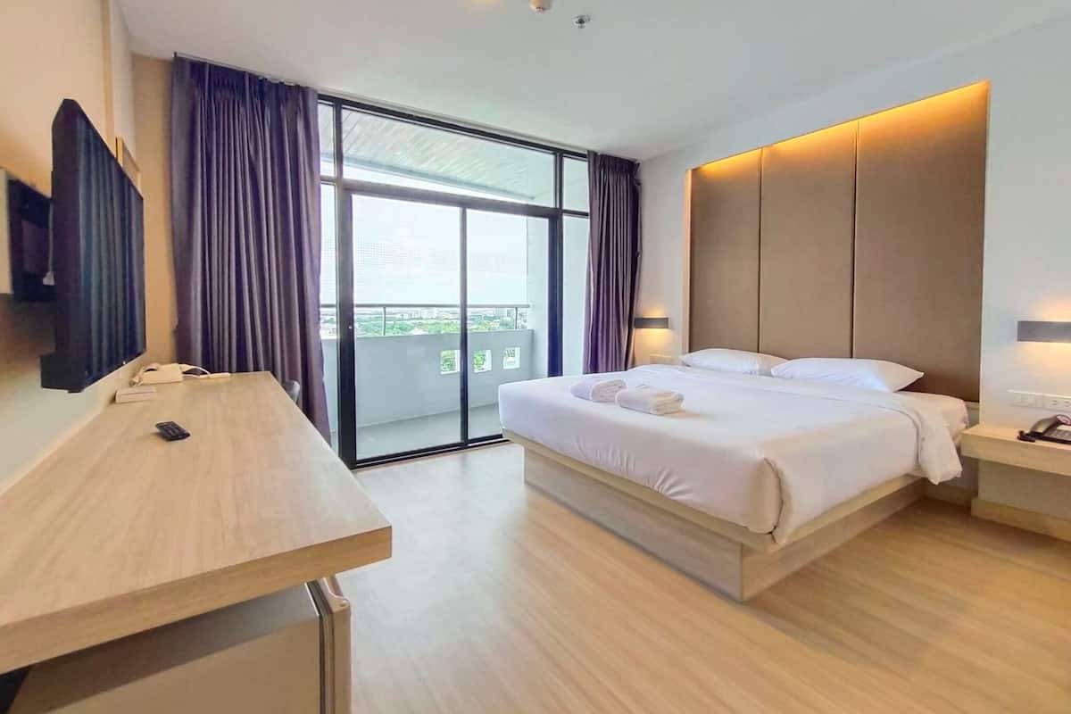 A modern hotel room with a large bed, a desk, a flat-screen TV, and a balcony with curtains.