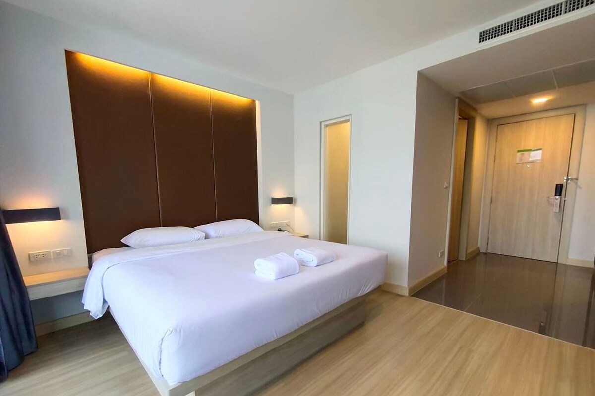 A modern hotel room with a large bed, bedside tables, a headboard, and a door.
