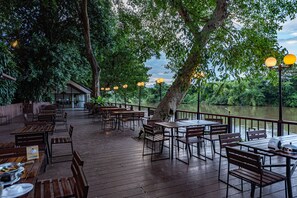 Un espace de restauration en plein air, avec des tables et des bancs en bois, entouré d’arbres et offrant une vue sur un plan d’eau.
