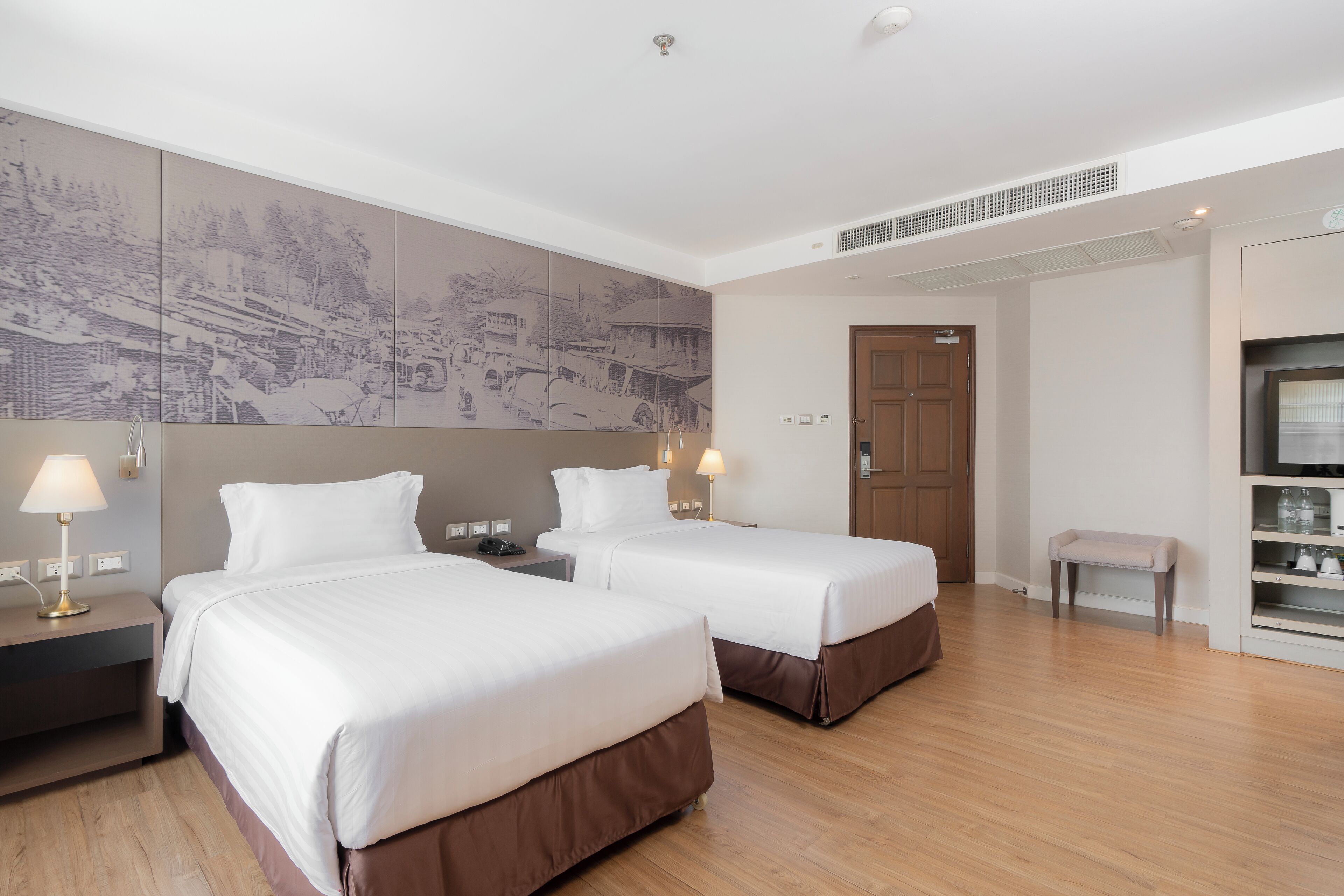 Une chambre d’hôtel avec deux lits, une grande œuvre d’art accrochée au mur, un petit banc et un meuble pour la télévision.
