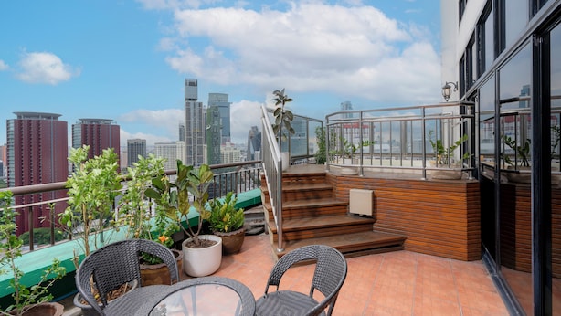 A rooftop terrace with potted plants, wicker chairs, and a glass table. - Grand Diamond Suite (Bangkok)