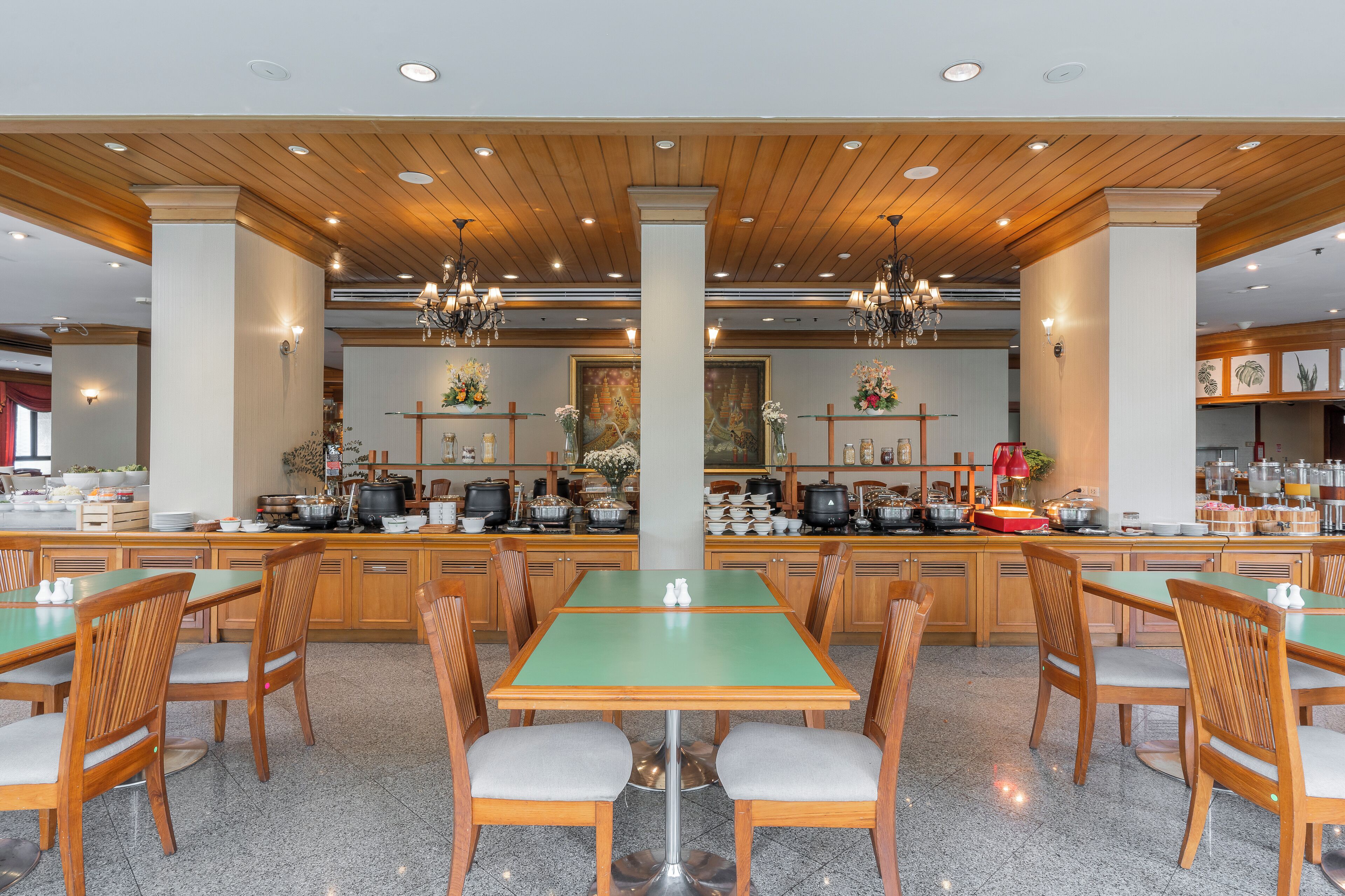 Un vaste espace dédié à la salle à manger, avec des tables et des chaises en bois, une colonne centrale et une cuisine en arrière-plan.