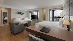 A modern hotel room with a large bed, a desk, a chair, a TV, and a city view. - Grand Diamond Suite (Bangkok)