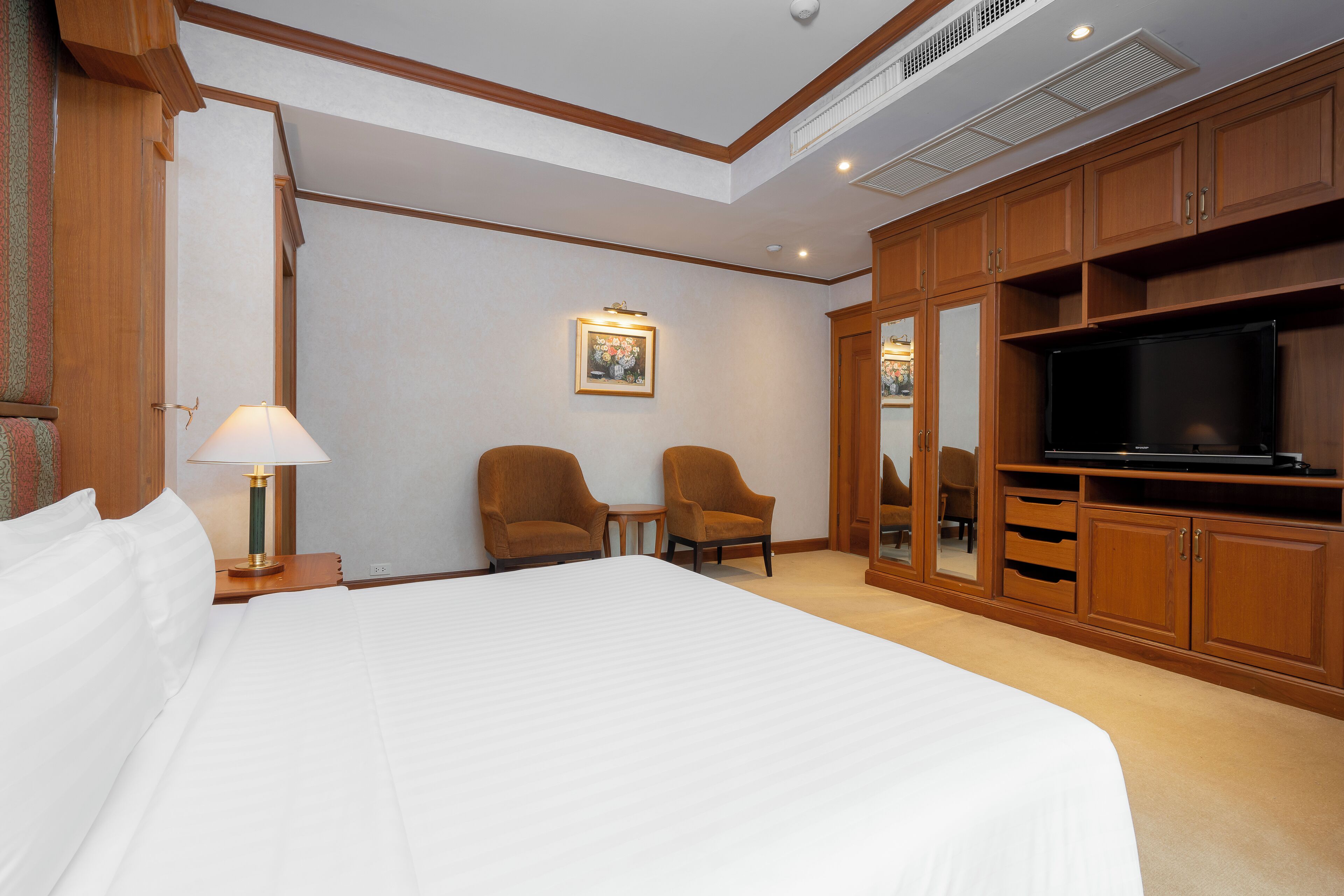 A hotel room with a large bed, two armchairs, a television, and wooden cabinets.