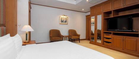 A hotel room with a large bed, two armchairs, a television, and wooden cabinets.