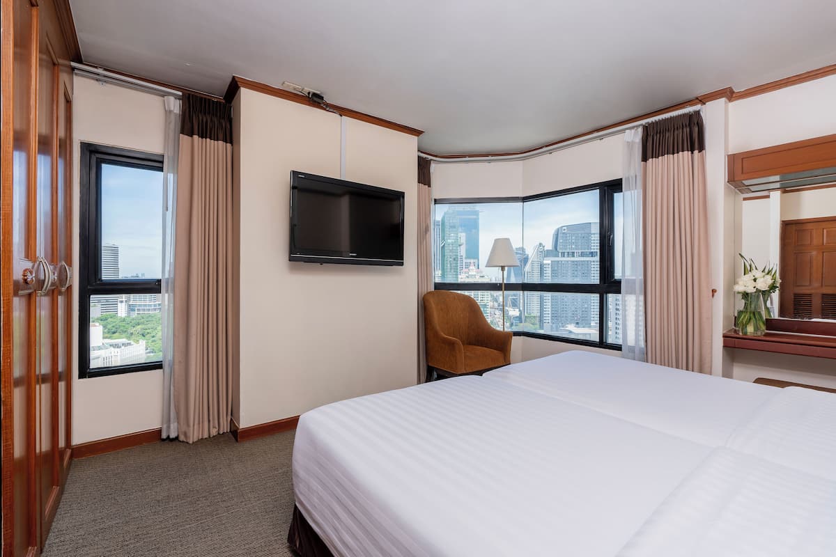 A hotel room with a large bed, a flat-screen TV, a chair, and a view of the cityscape through large windows.