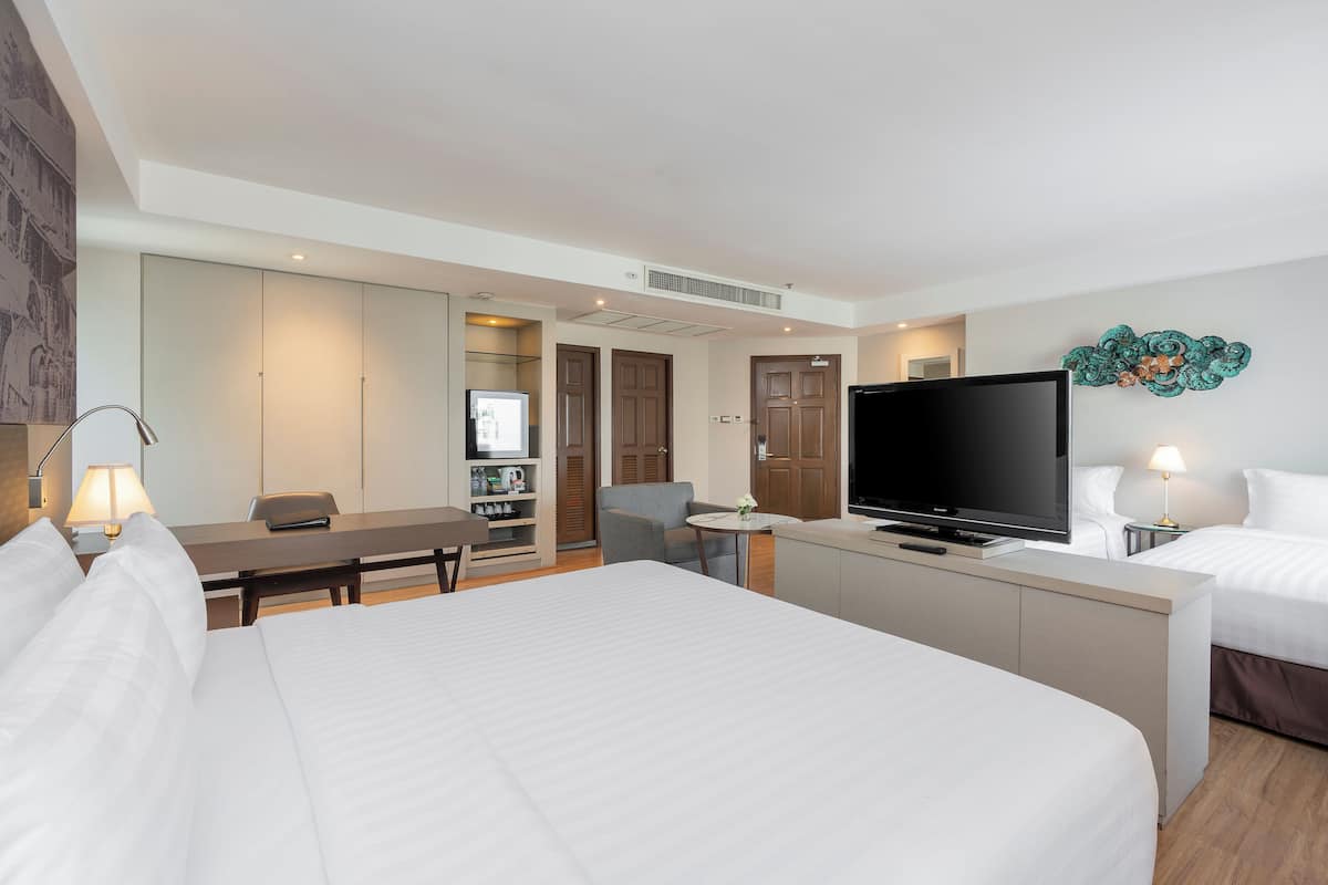 A hotel room with a large bed, a desk with a chair, a television, and a small table with a lamp.