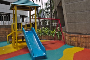 Kids can play on the slide and play structure in this outdoor play area surrounded by a low wall and colorful play surface.