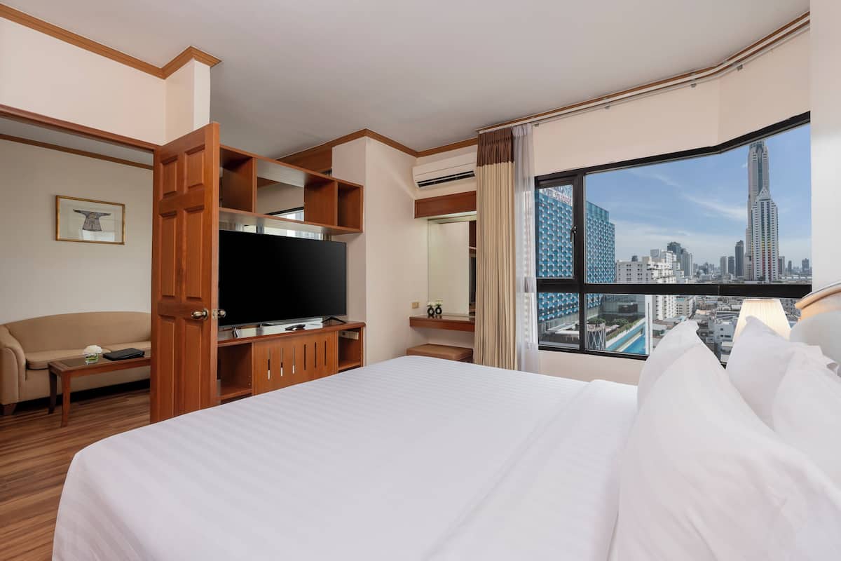 A hotel room with a large bed, a television, a wooden cabinet, and a city view through a large window.