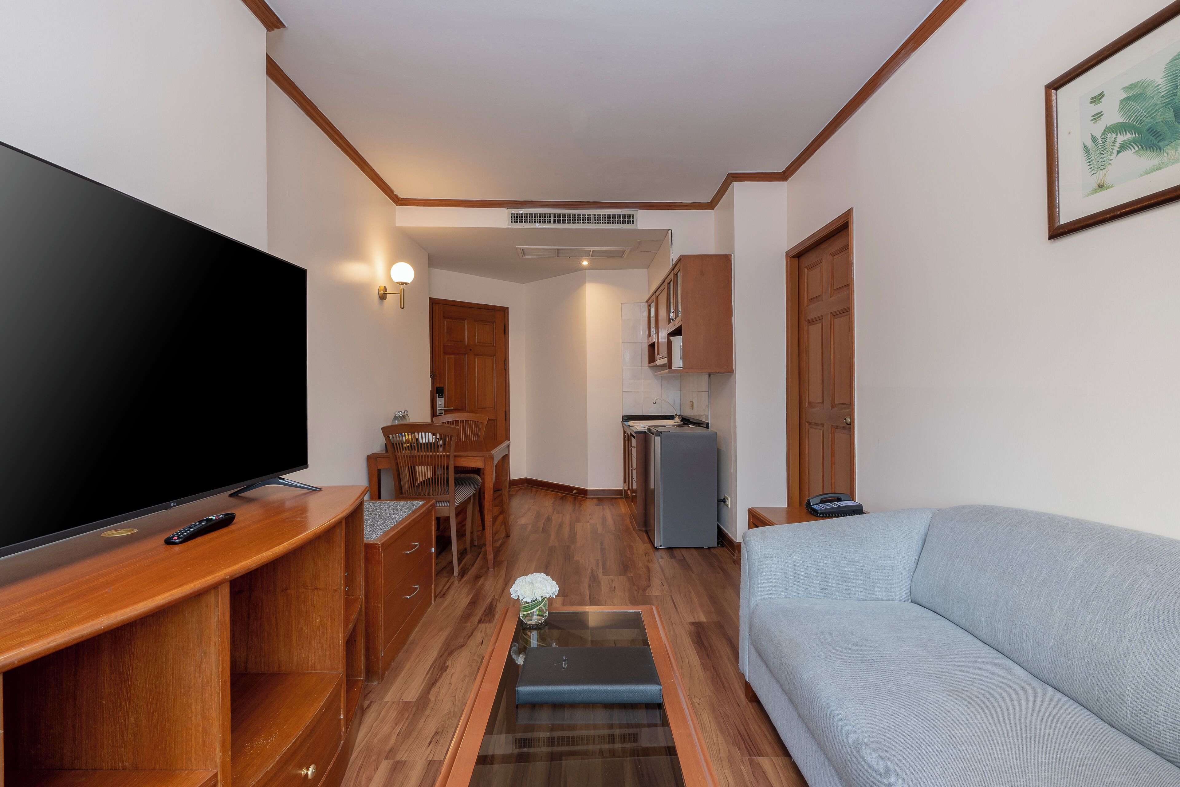 Ein gemütlicher Wohnraum mit Flachbildfernseher, Holzmöbeln, einer Couch und einer Küchenzeile.